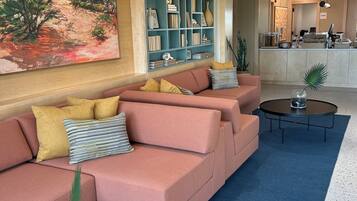 A modern lobby with a pink sofa, a bookshelf, a coffee table, and a reception desk.