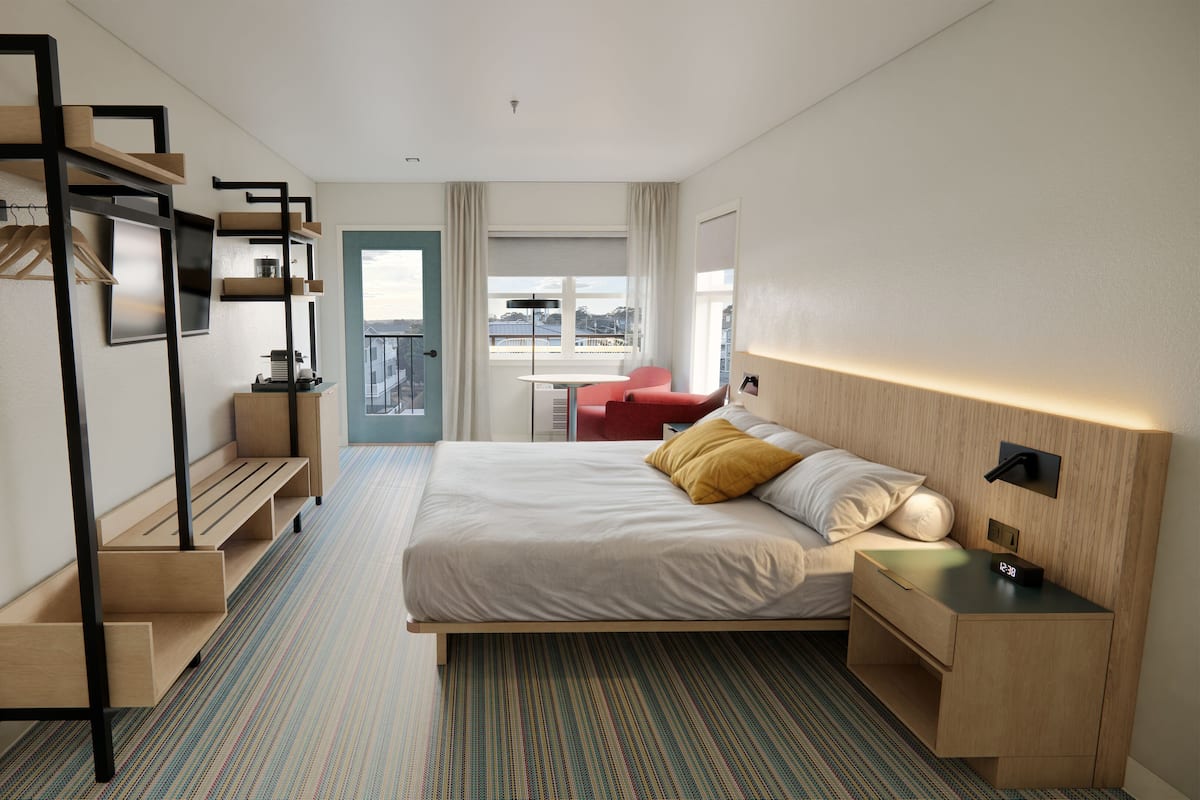 Habitación de hotel moderna con cama, escritorio, silla, una mesita y vistas a la ciudad a través del ventanal.