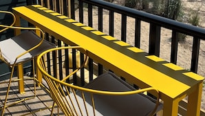 Un balcón con mobiliario amarillo que da a una playa con dunas y el océano.
