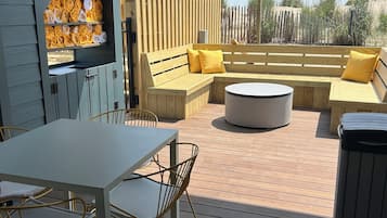 An outdoor patio with a wooden table and chairs, a sofa with yellow cushions, and a round coffee table.