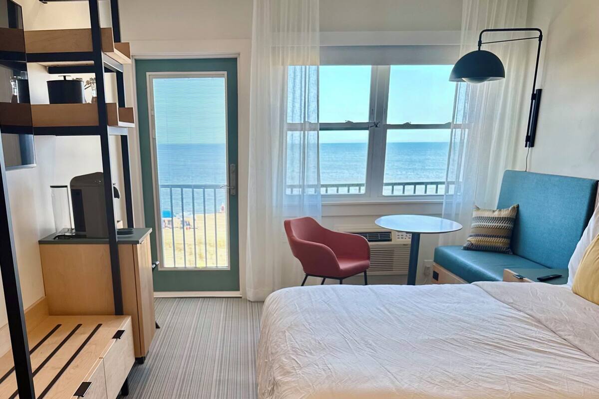 Una habitación de hotel con una cama grande, un escritorio, una silla, una mesita, un sofá y un balcón con vistas al mar.