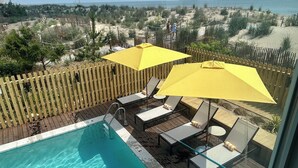 Un área de piscina con muelle de madera, sombrillas amarillas y sillones de descanso.