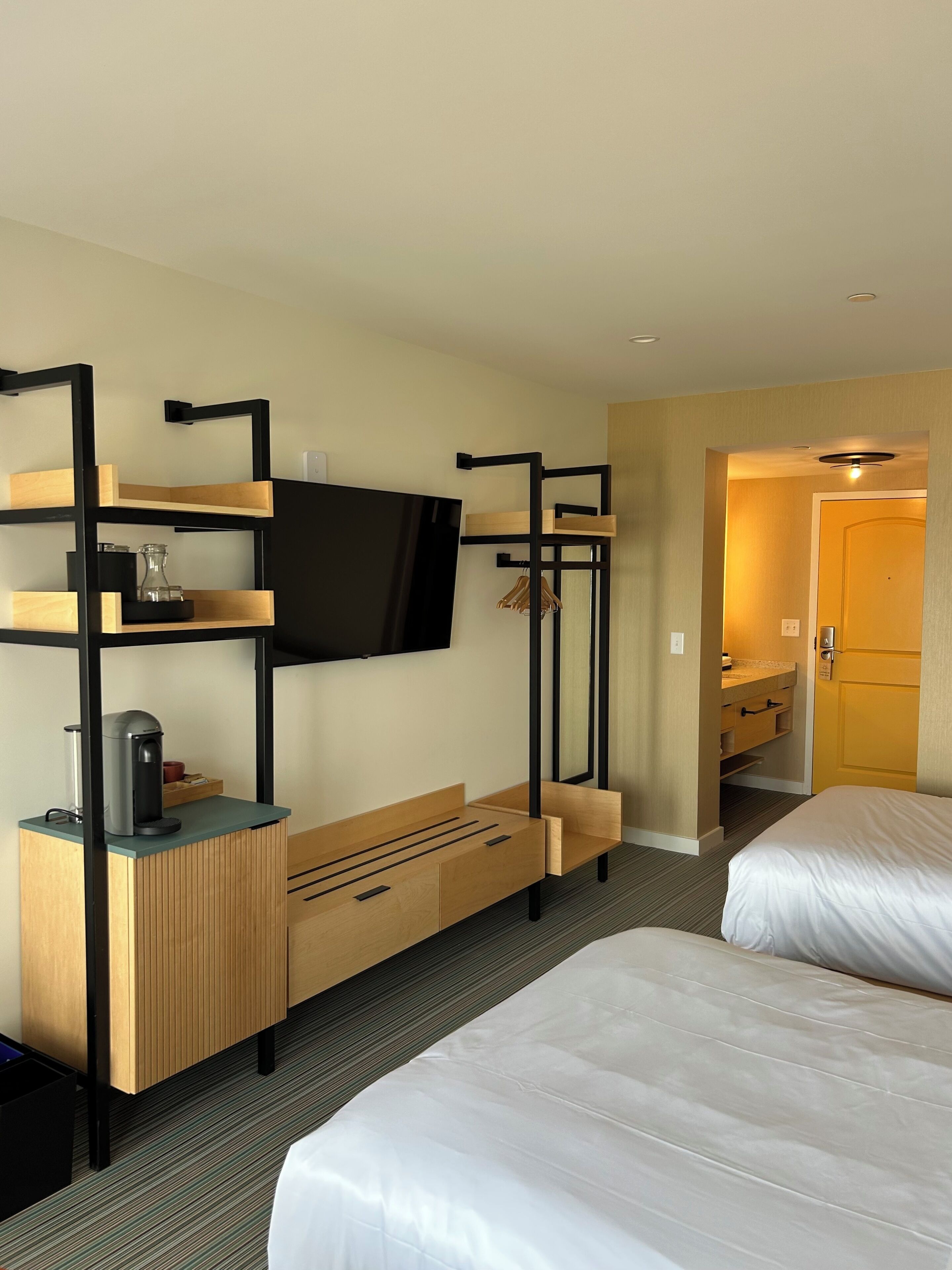 Une chambre d’hôtel avec des lits superposés, un téléviseur fixé au mur, une machine à café et un bureau en bois avec des tiroirs.