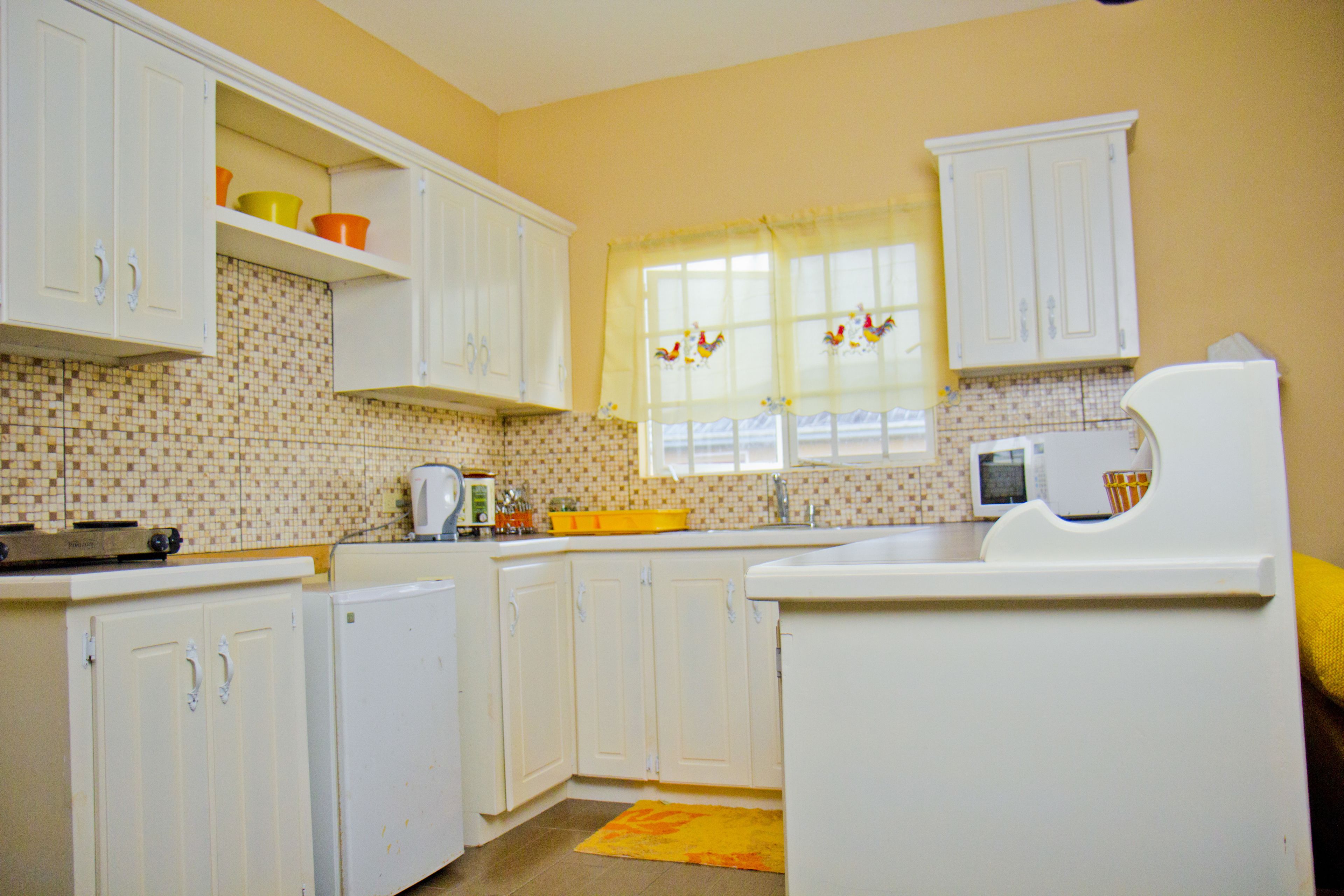 A kitchen with white cabinets, a microwave, and a window with curtains.