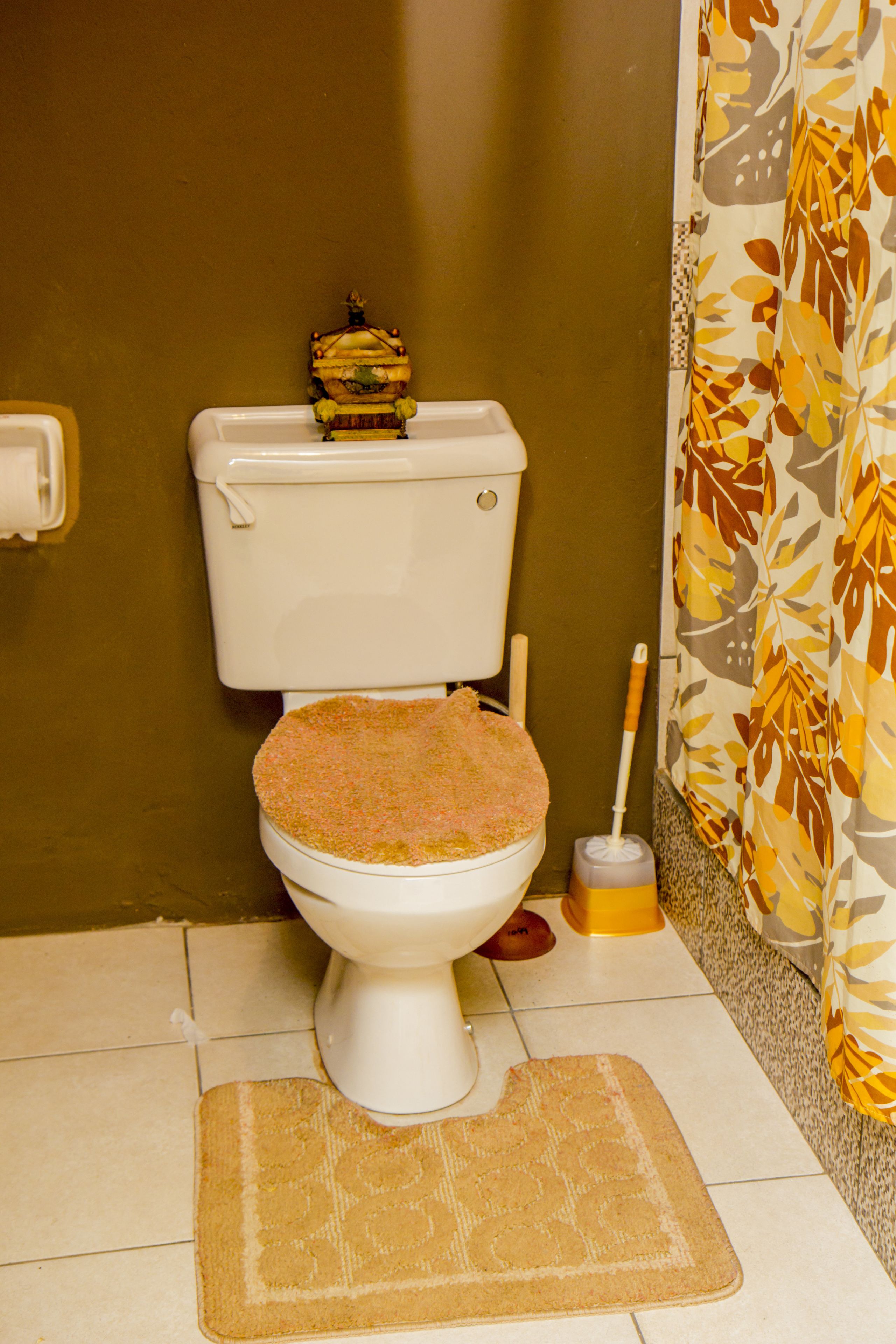A toilet with a decorative basket on top, a toilet brush, and a patterned shower curtain.