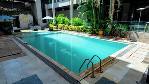 Ein Schwimmbecken mit gefliestem Sonnendeck, umgeben von Grünpflanzen und einer Glasbarriere.