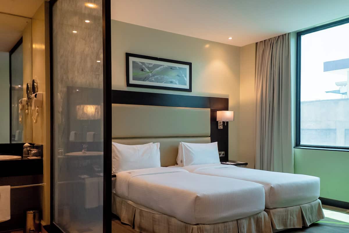 Habitación de hotel con una cama grande, una mesita de noche, un espejo, una ventana con cortinas y un cuadro en la pared.