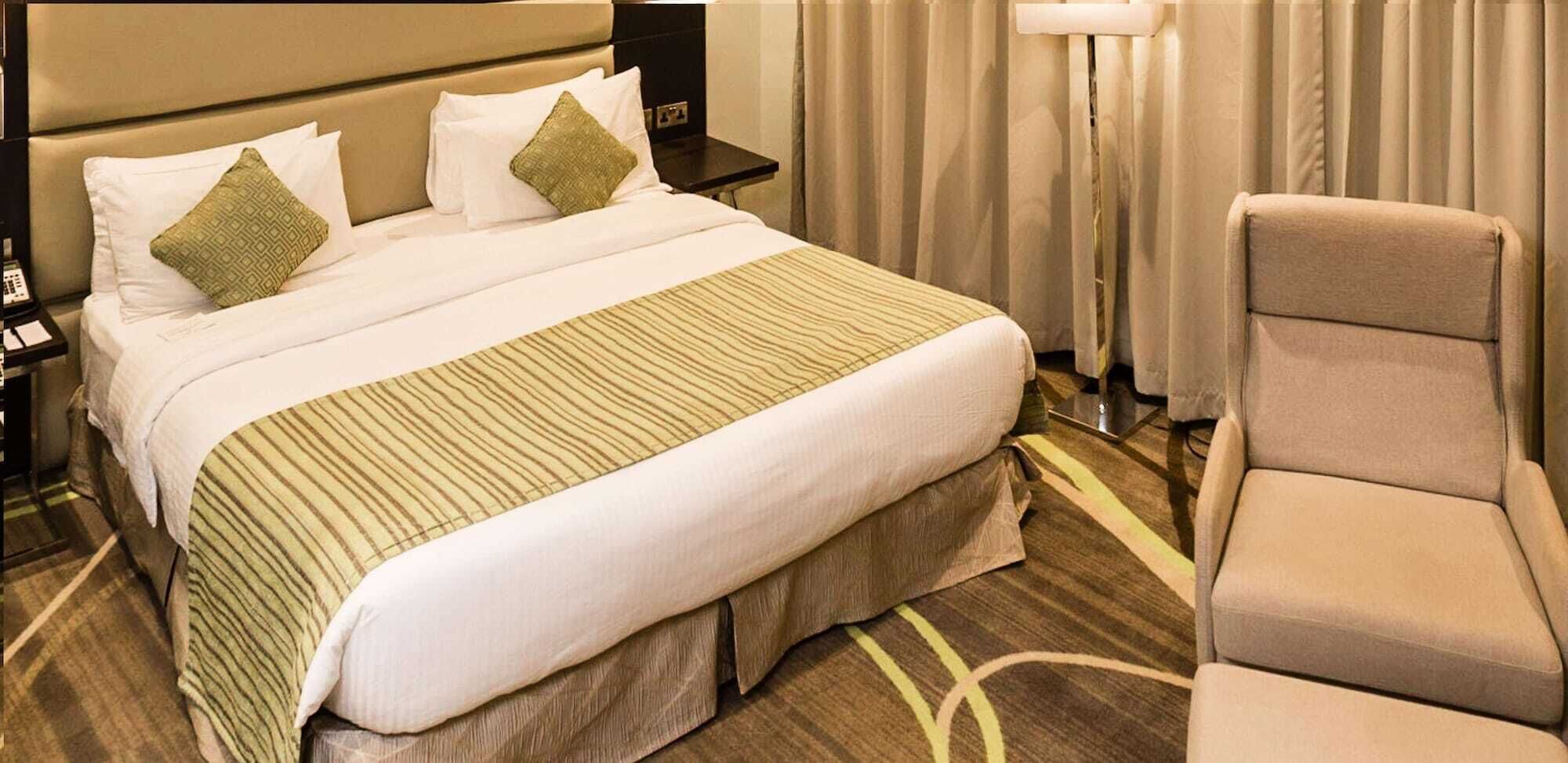 A hotel room with a large bed, a chair, and a nightstand with a phone.
