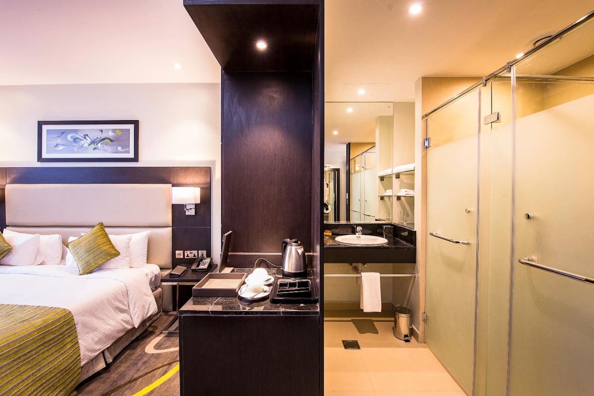 Una habitación de hotel con cama, escritorio, teléfono, hervidor y lavamanos en el baño.