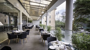Ein Restaurant mit Sitzgelegenheiten auf dem Dach, Tische, Stühle, Glasgeländern und Blick auf die Stadt.