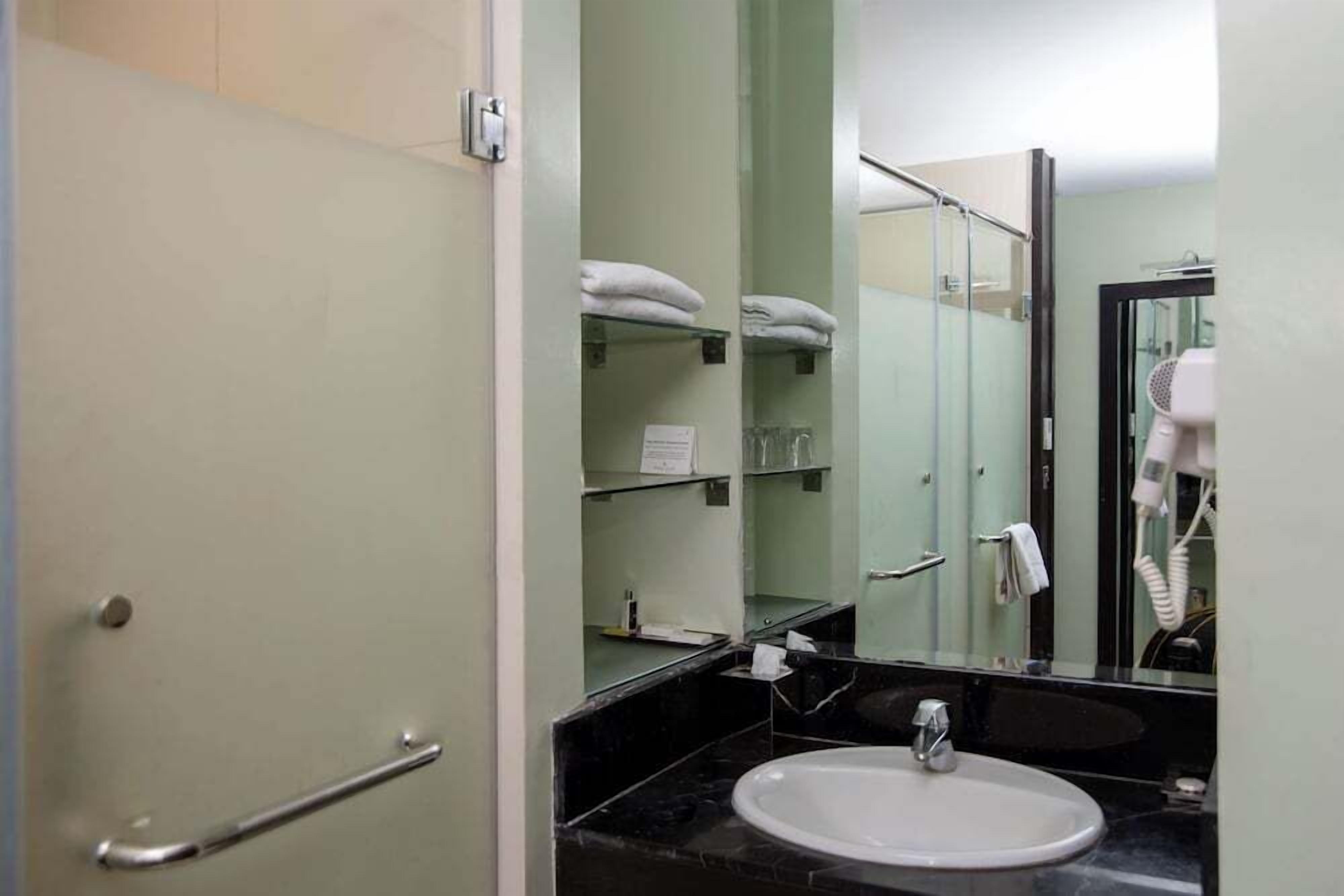 Un baño con lavamanos blanco, cabina de ducha de vidrio y toallero con toallas dobladas.