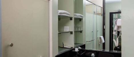 Un baño con lavamanos blanco, cabina de ducha de vidrio y toallero con toallas dobladas.