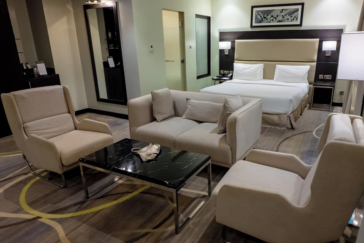 Habitación de hotel con cama, dos sillones, un sofá, una mesa de centro y un escritorio con lámpara.