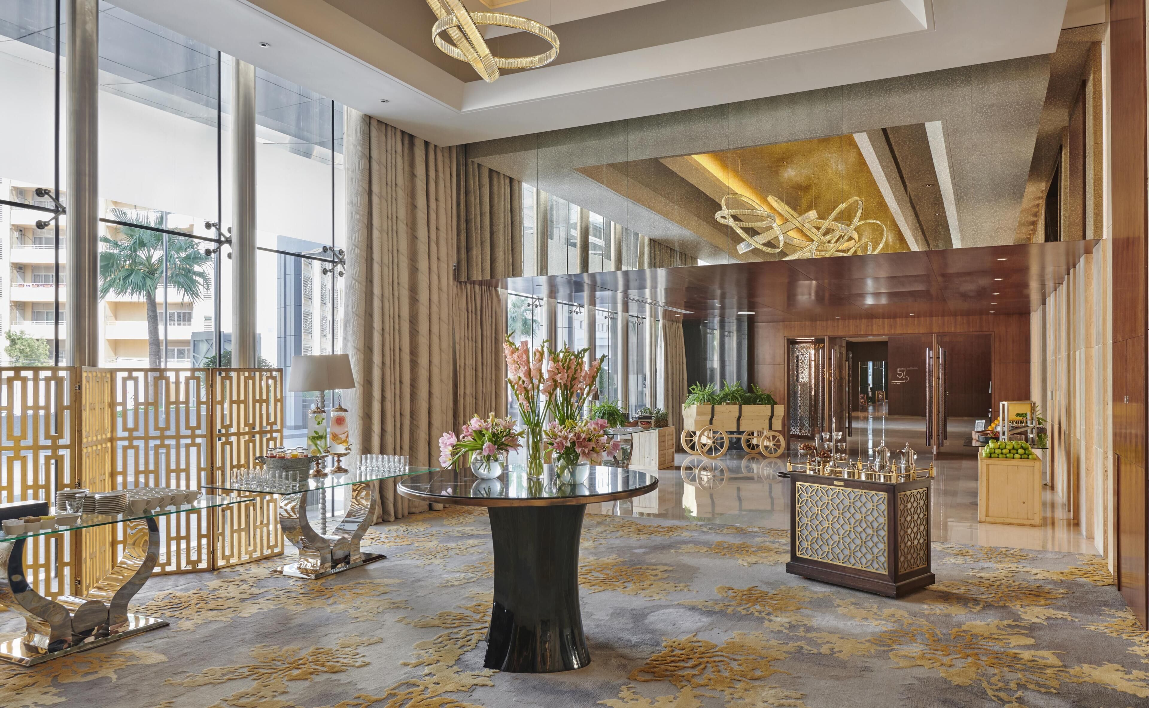 A spacious lobby with a central round table, a reception desk, and large windows offering views of the city.