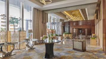 A spacious lobby with a central round table, a reception desk, and large windows offering views of the city.
