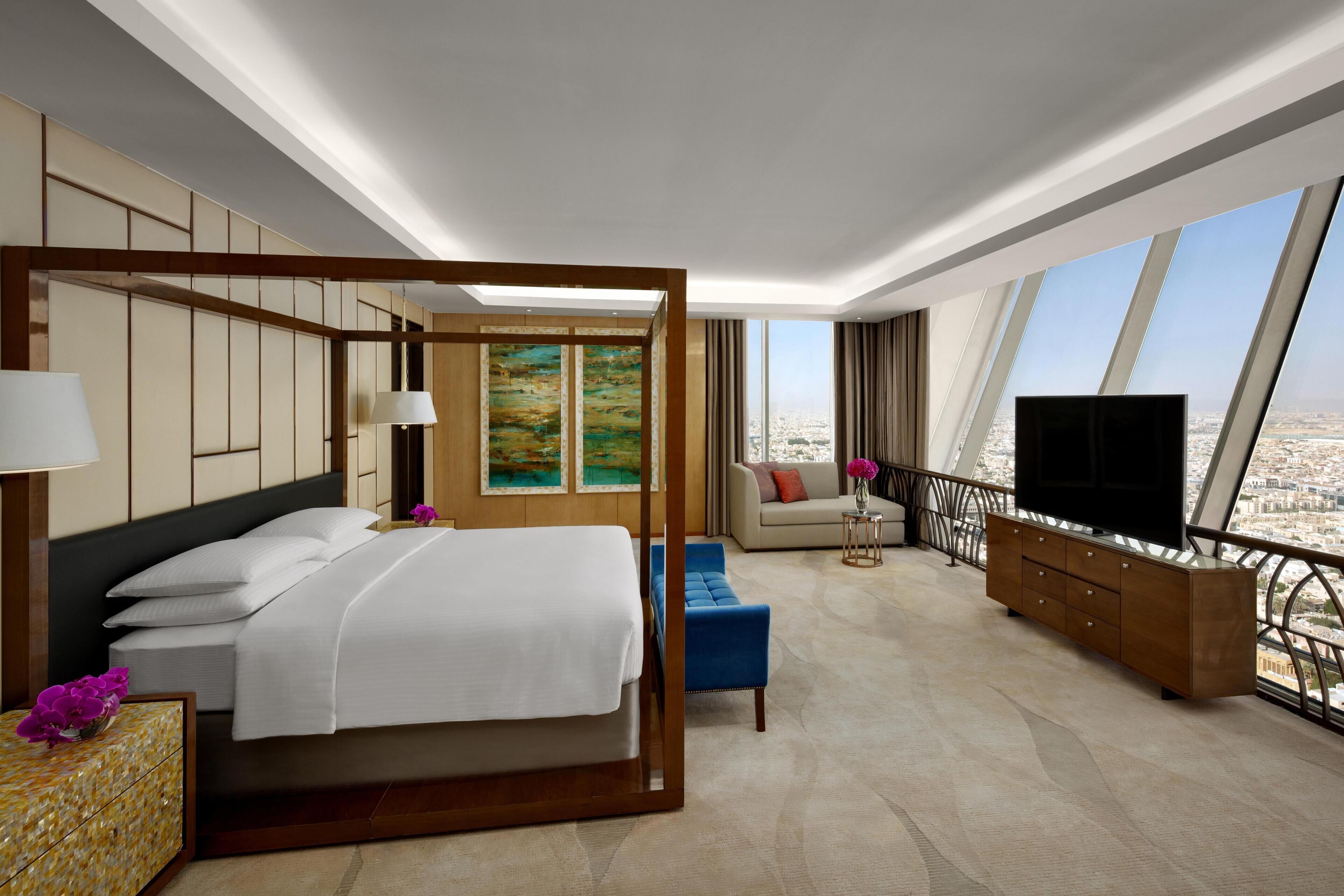 Una habitación de hotel moderna con una cama grande, un sofá, un televisor y vistas a la ciudad.