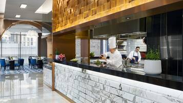A modern restaurant with marble countertops, a chef preparing food, and a seating area with blue chairs.