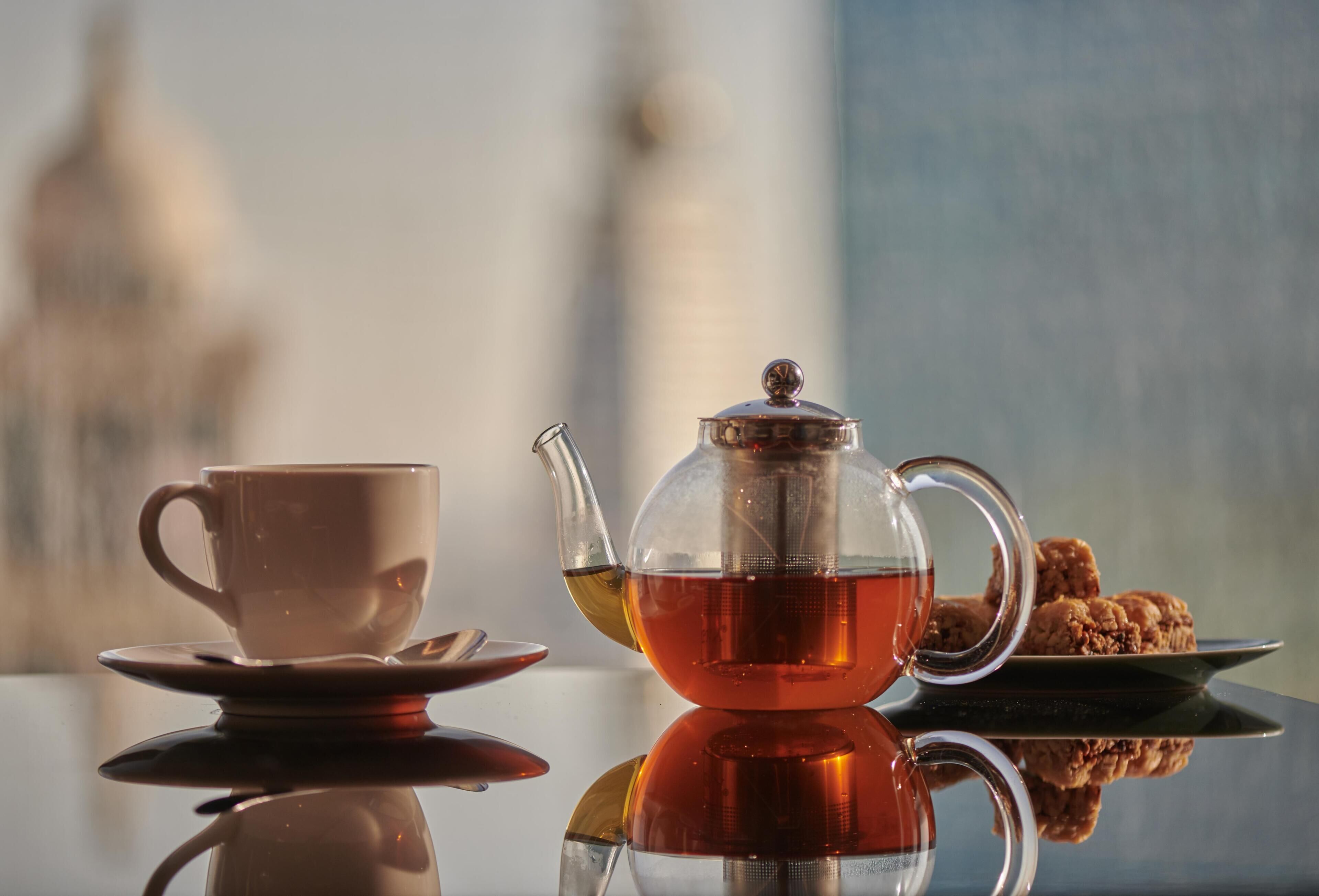 A tea set with a cup, saucer, and teapot on a reflective surface.