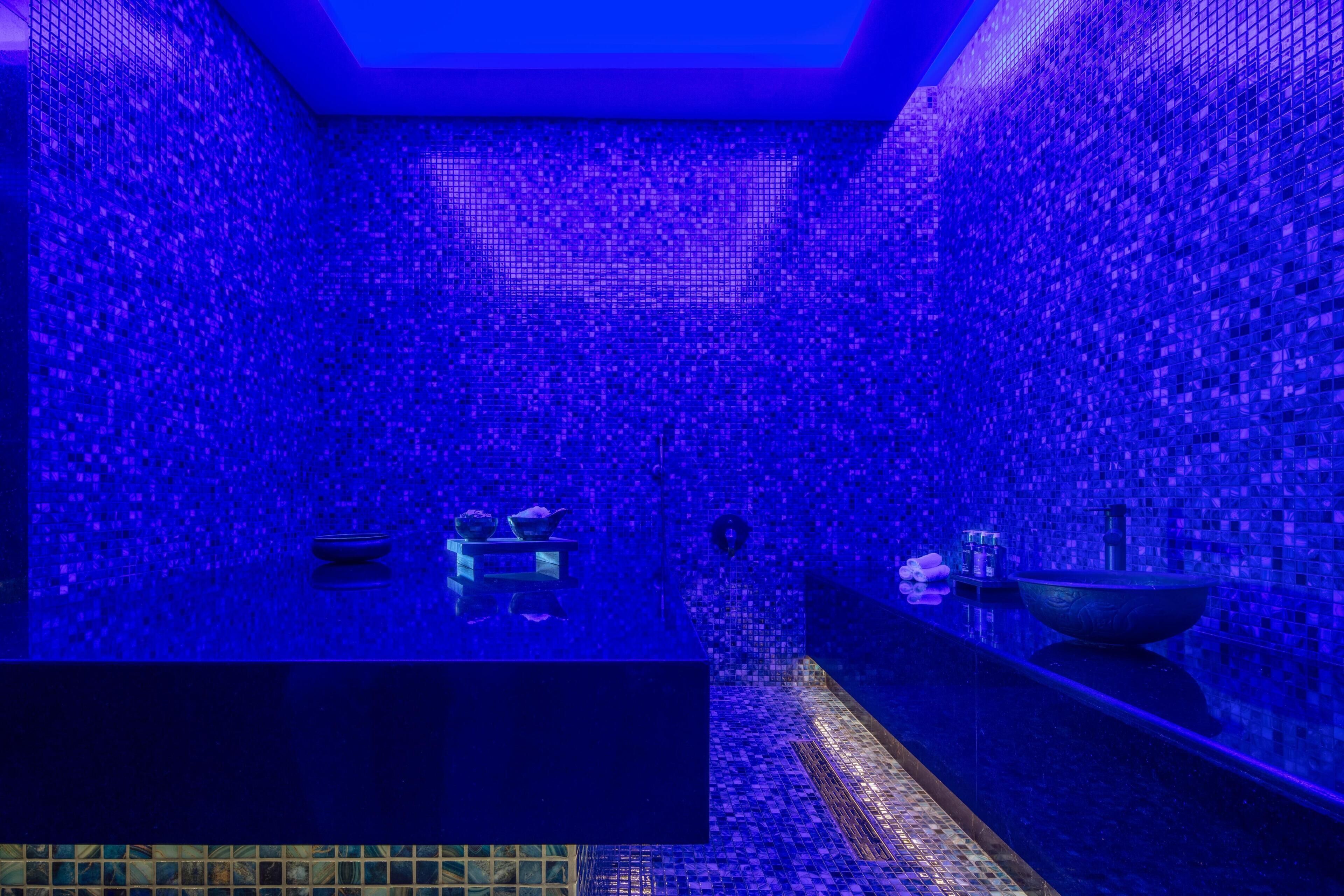 A bathroom with mosaic tile walls, a black countertop, and a large basin.