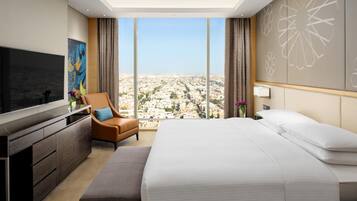 A modern hotel room with a large bed, a TV, a seating area, and a city view.
