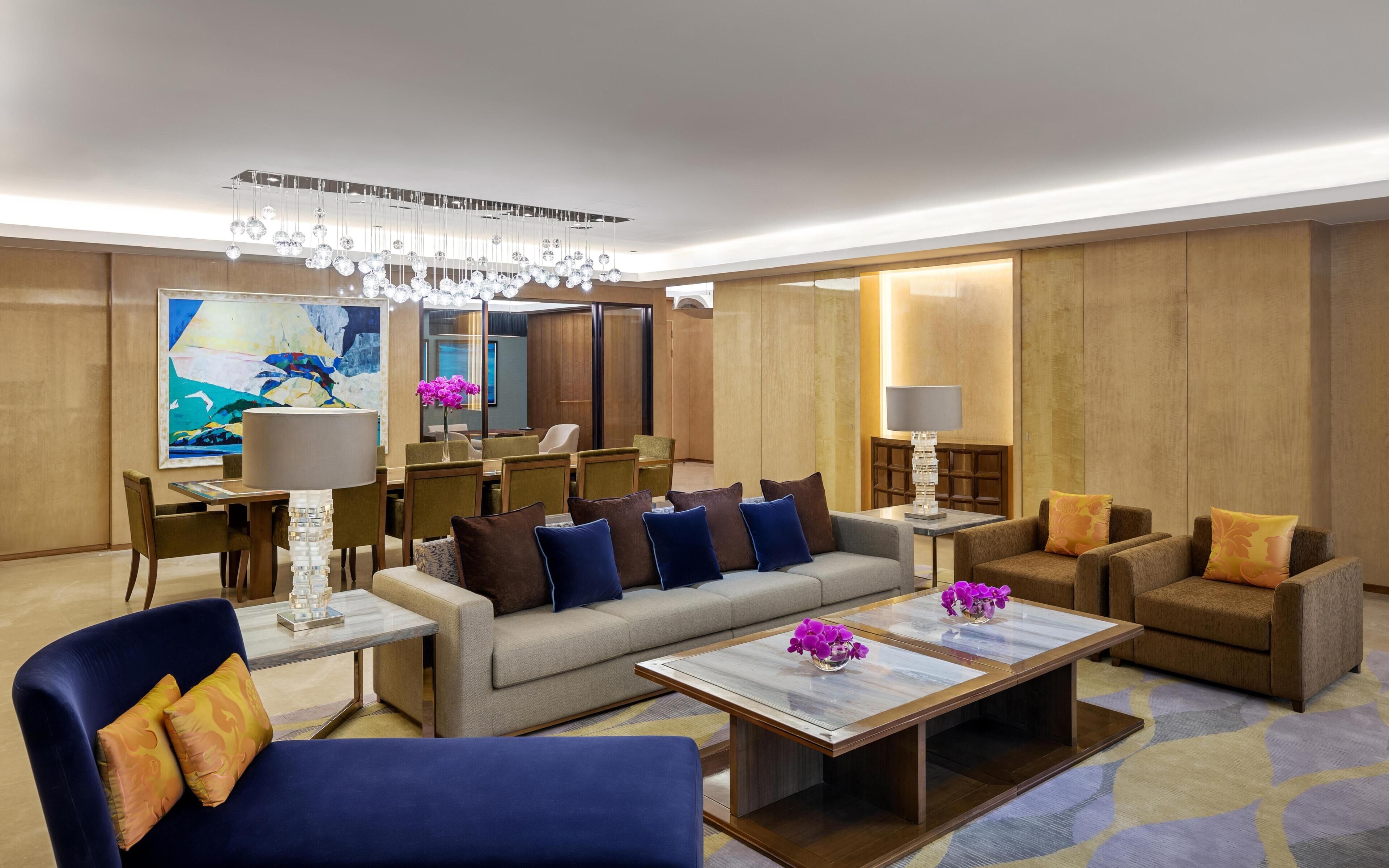Een moderne hotelhal met een bank, stoelen, een bijzettafeltje, een kroonluchter en een schilderij.