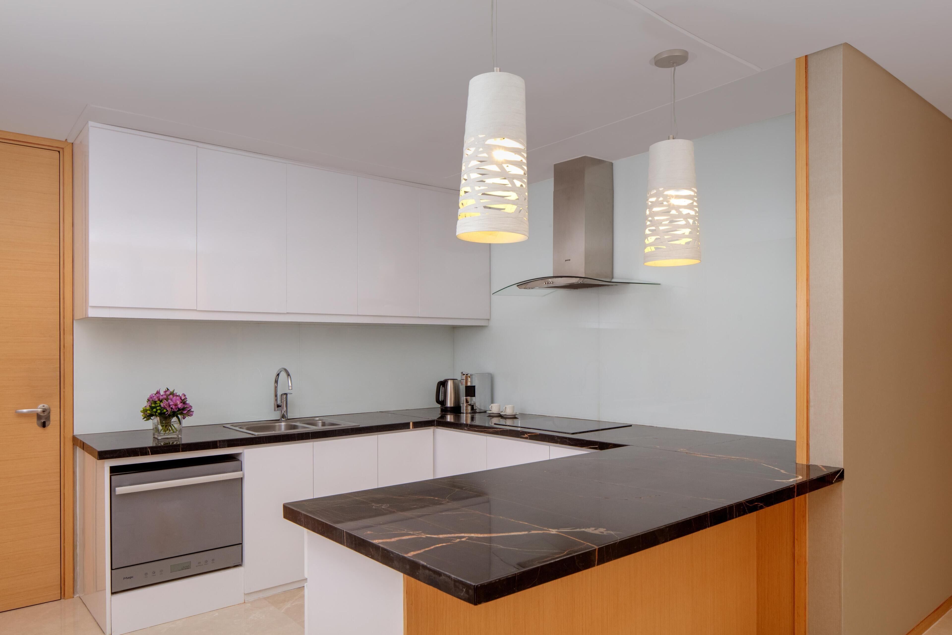 Une cuisine moderne avec des meubles blancs, un plan de travail en marbre noir et deux suspensions lumineuses.
