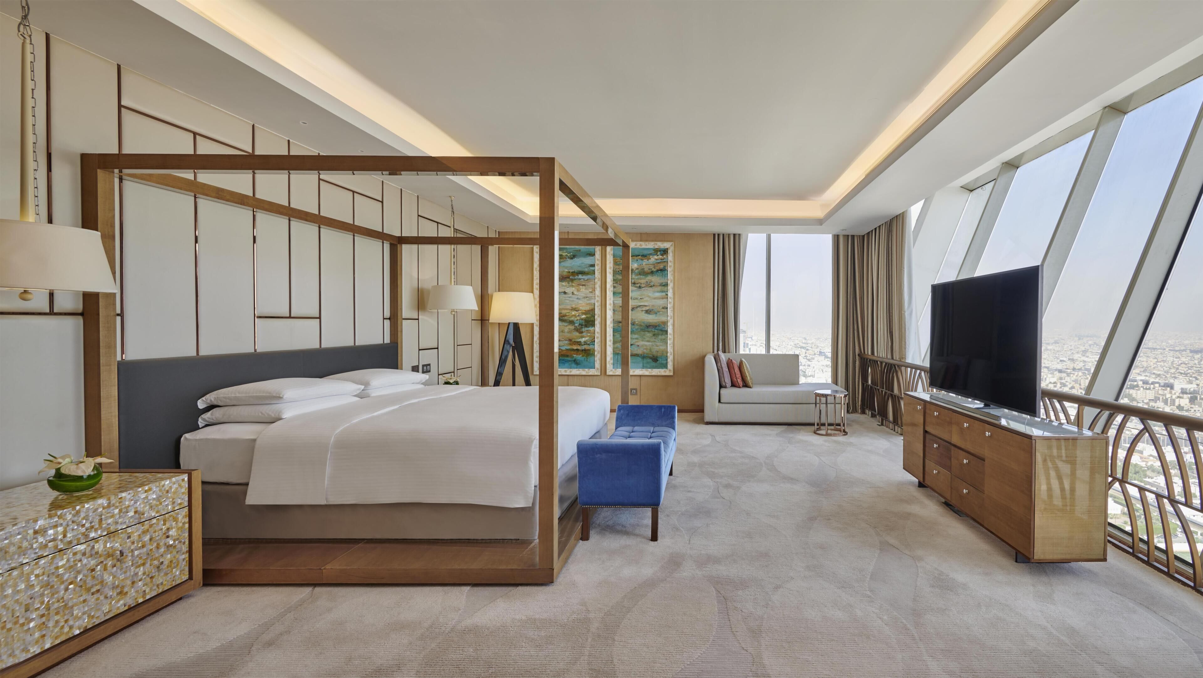 Una habitación de hotel moderna con cama con dosel, sofá, televisor y balcón con vistas a la ciudad.