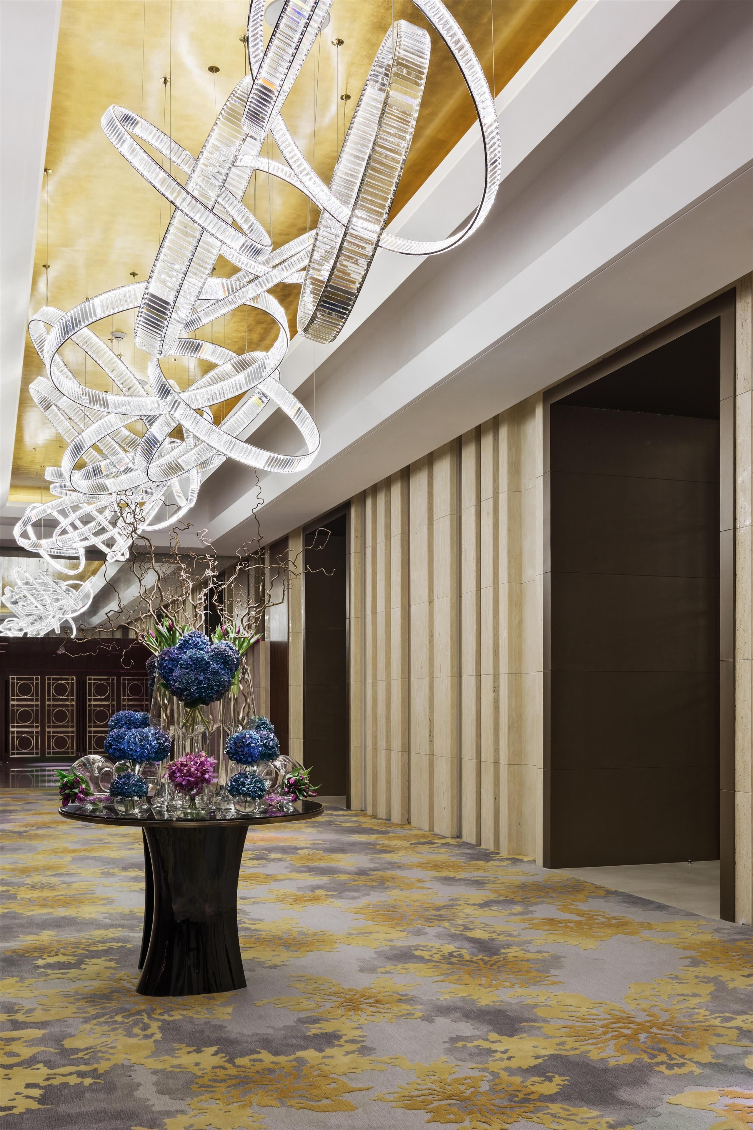 A lobby with a large, abstract light sculpture, a floral centerpiece, and a patterned carpet.