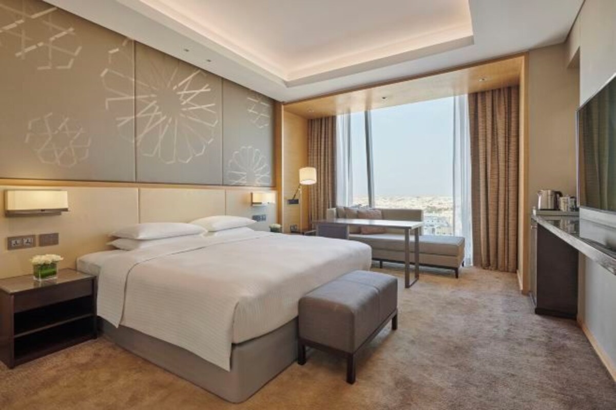 A modern hotel room with a large bed, a desk, and a view of the city.