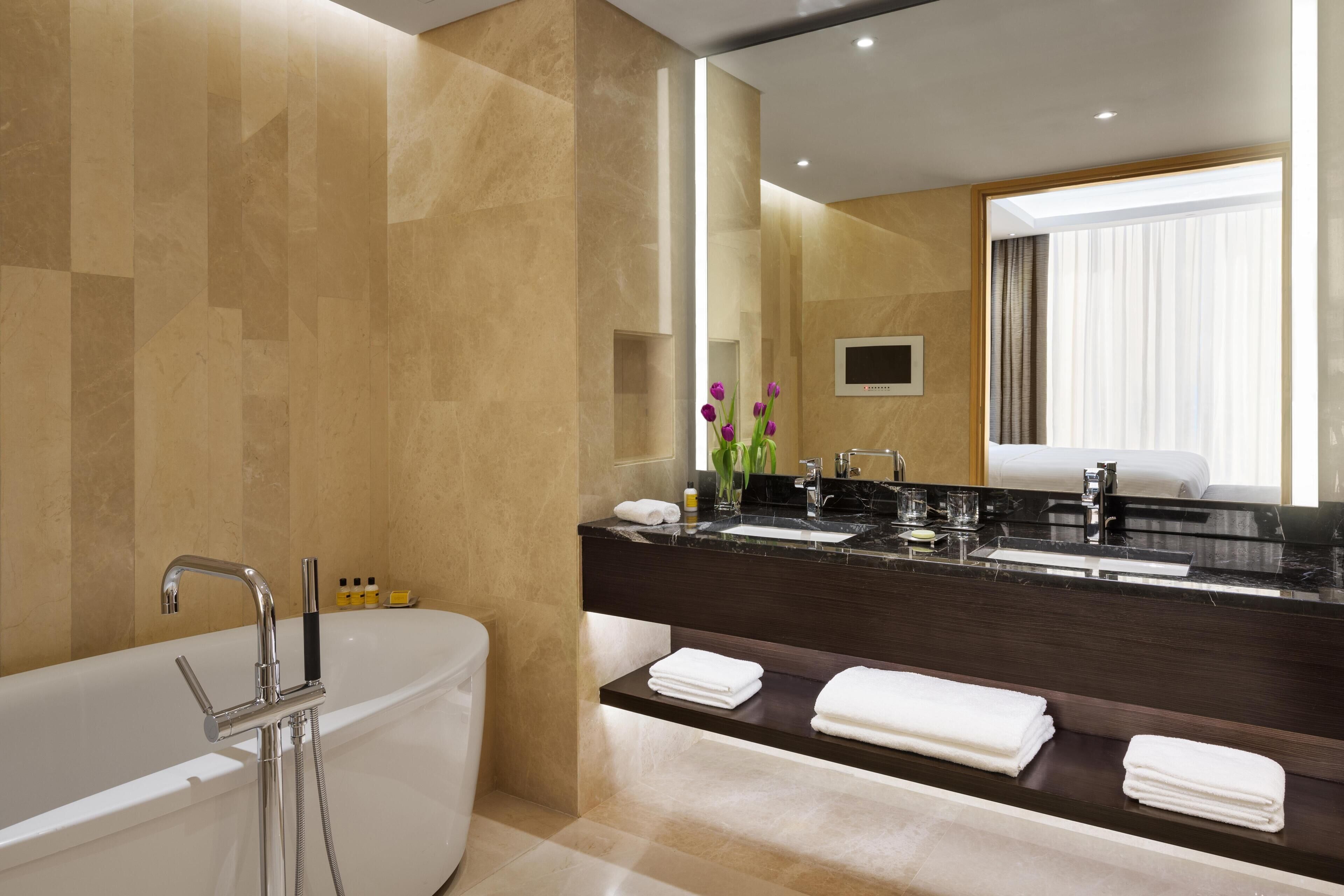 Un baño moderno con bañera, lavamanos doble y un espejo grande.