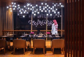A restaurant with tables, chairs, and a view of the city at night.