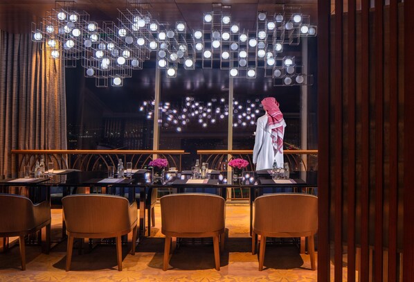 A restaurant with tables, chairs, and a view of the city at night.