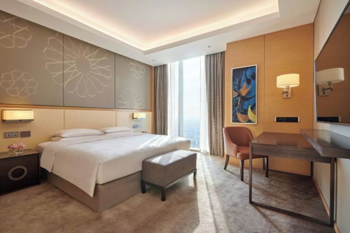 A modern hotel room with a large bed, a desk, and a view of the city.