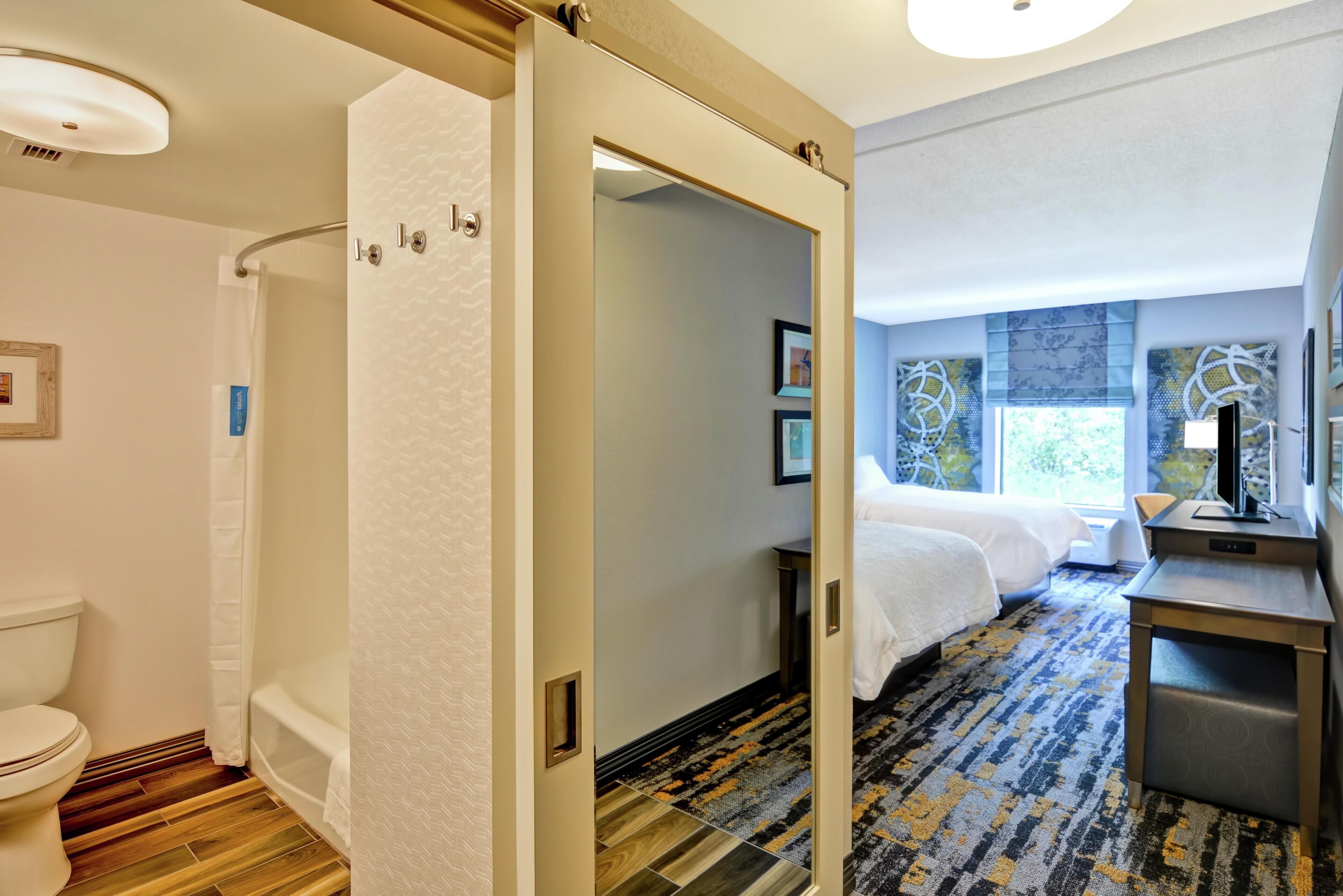 Une chambre d’hôtel équipée d’une douche, de toilettes, d’un lit, d’un bureau et offrant une vue sur l’extérieur.