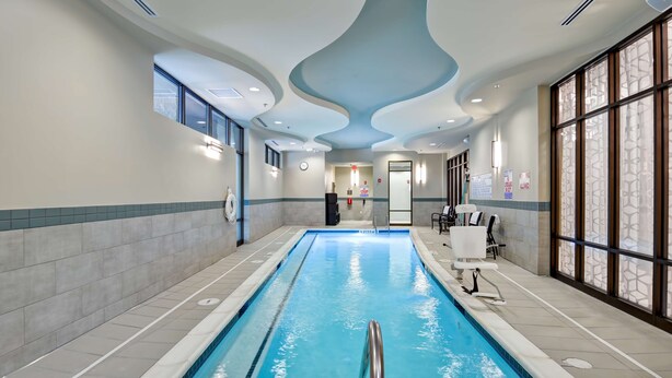 Una piscina interior con vistas claras al diseño del techo, paredes con azulejos y una zona de estar con sillas y una mesa.