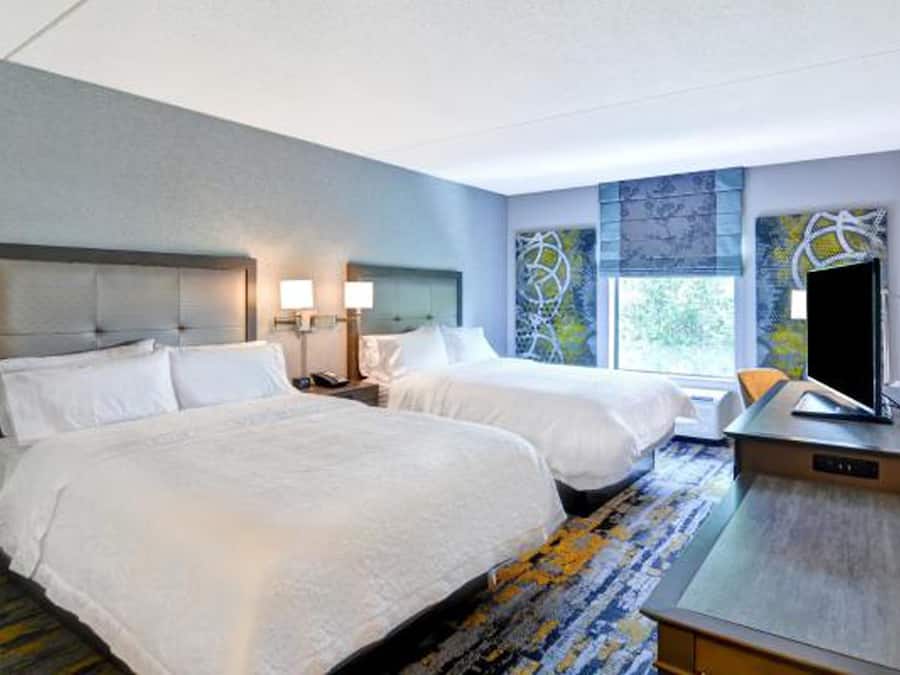 A hotel room with two beds, a desk, and a television.