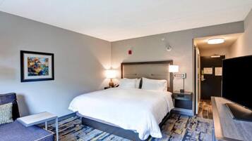 A hotel room with a large bed, a desk, a chair, a TV, and a painting on the wall.