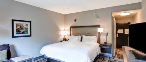 Una camera d'albergo con un ampio letto, una scrivania, una sedia, una televisione e un quadro appeso al muro.