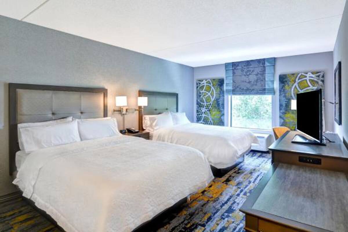 A hotel room with two beds, a desk, a TV, and a window with a view.