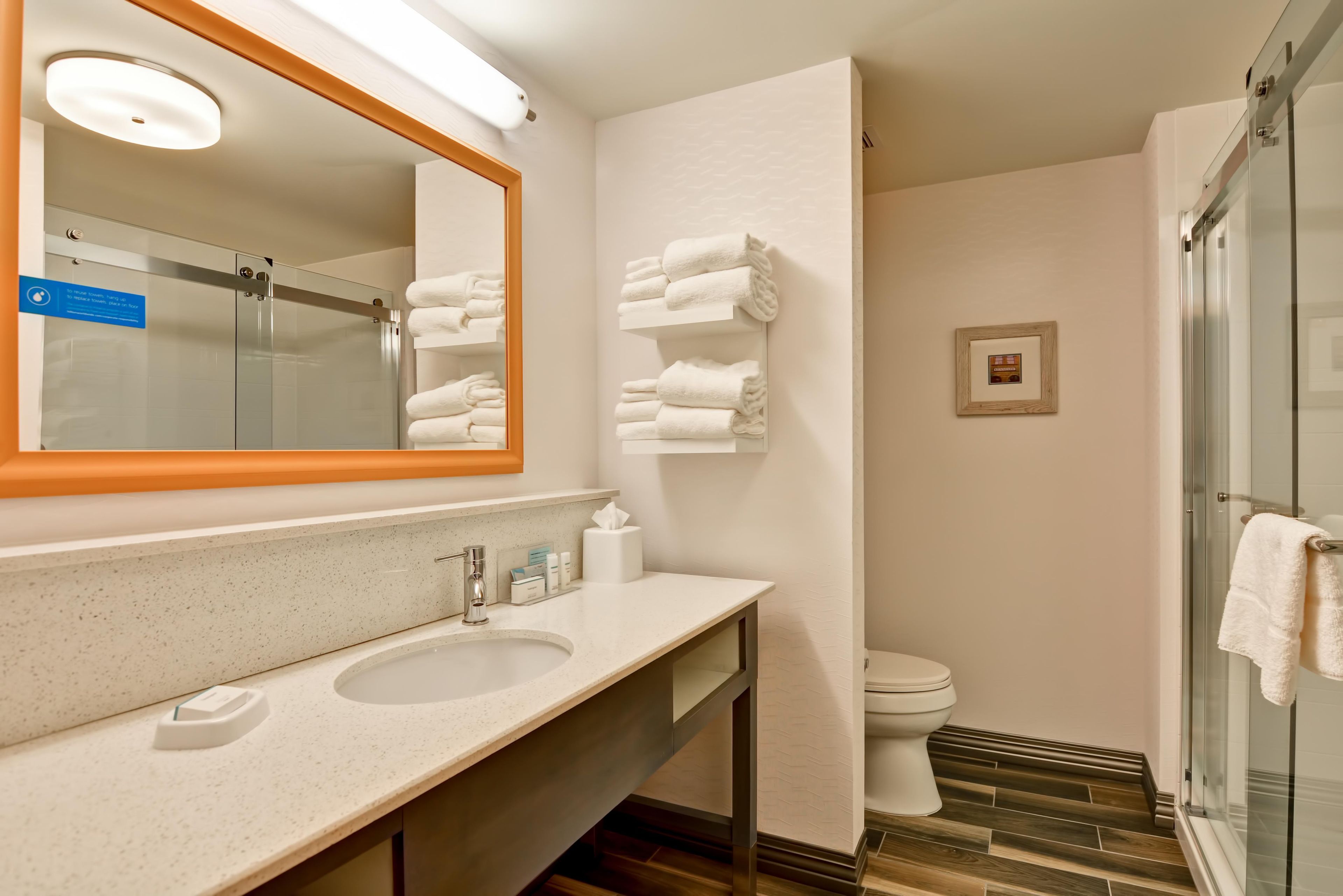 A modern bathroom with a large mirror, two sinks, a toilet, and a shower area.
