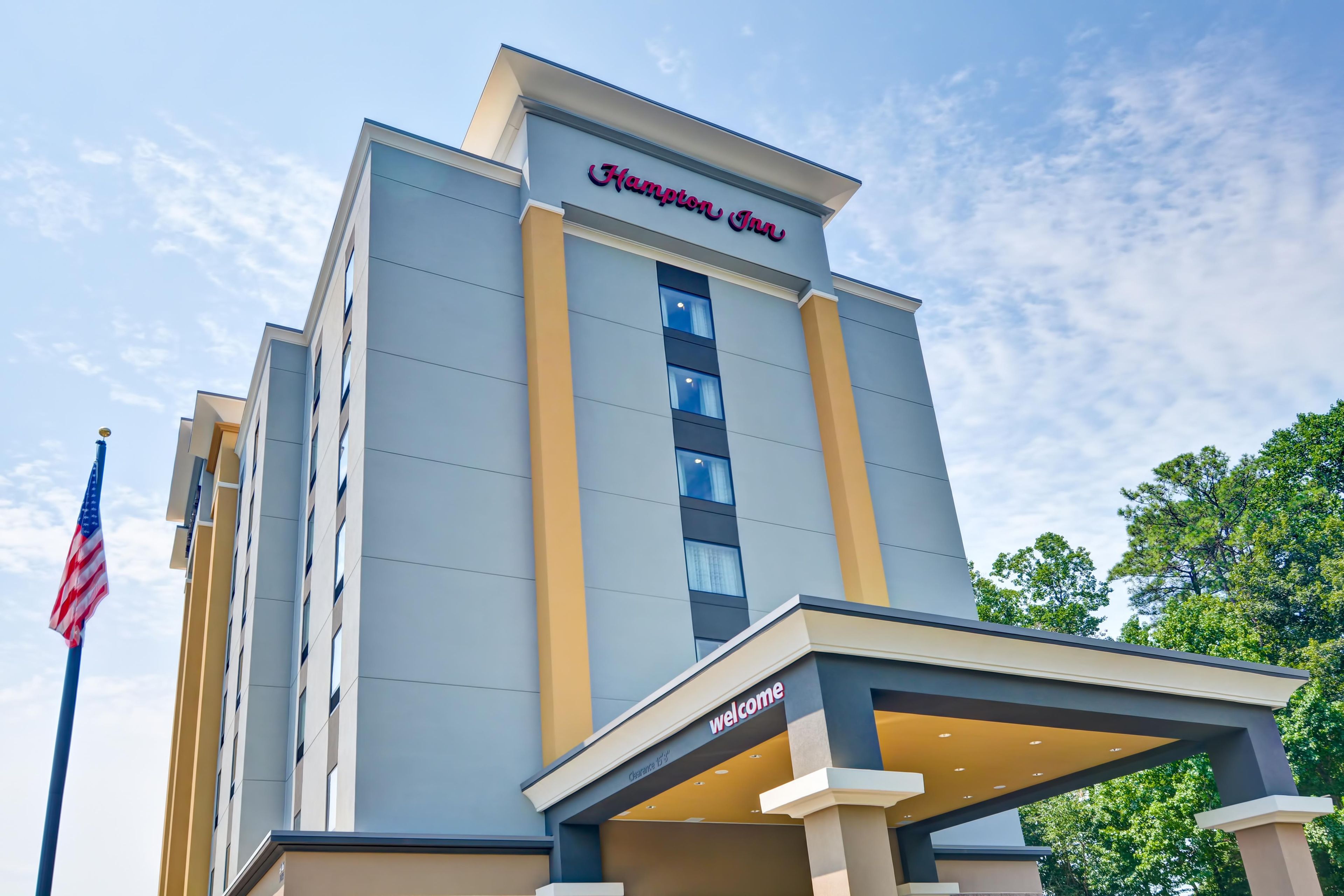 A hotel with a modern facade, a prominent sign reading 'Hampton Inn,' and a welcoming entrance with a 'Welcome' sign.