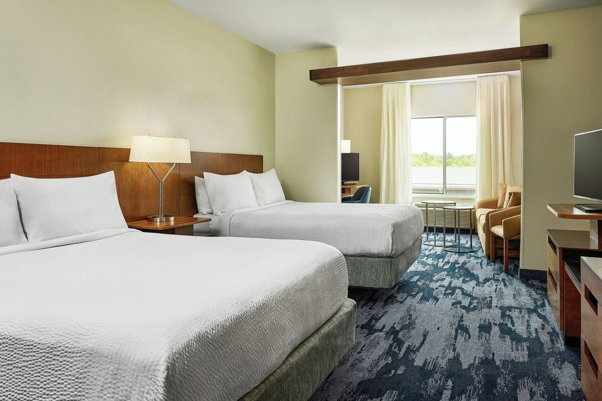 A hotel room with two beds, a desk, a chair, a TV, and a window with curtains.