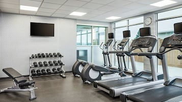 Ein Fitnessstudio mit Laufbändern, Gewichten und einer Trainingsbank.