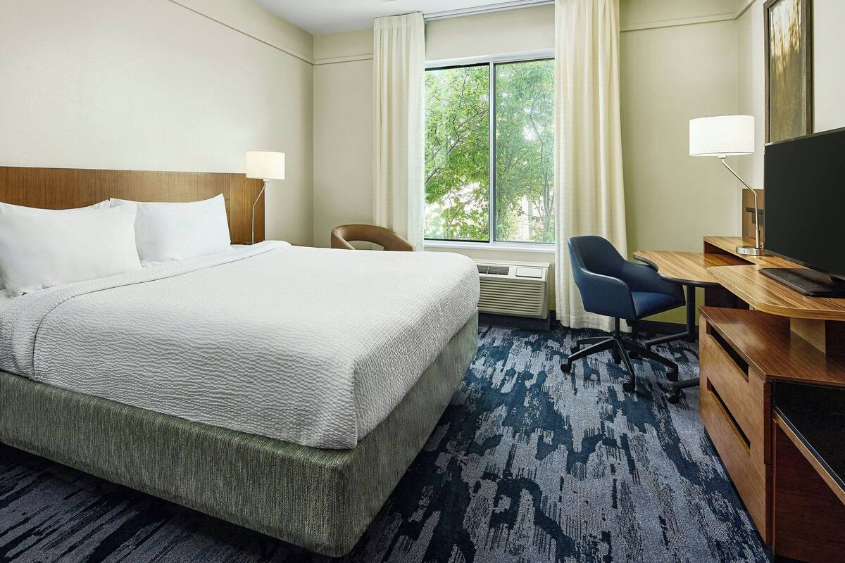A hotel room with a large bed, a desk with a chair, a television, and a window with curtains.