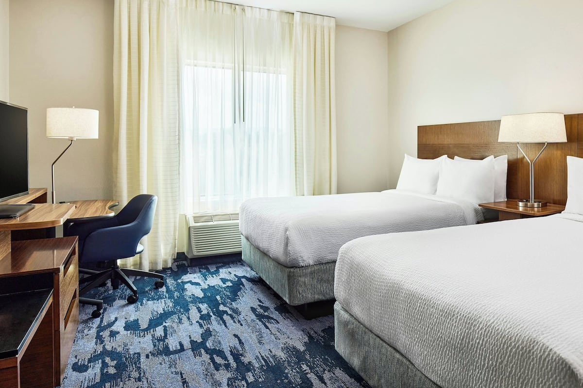 A hotel room with two beds, a desk with a chair, a TV, and a lamp.