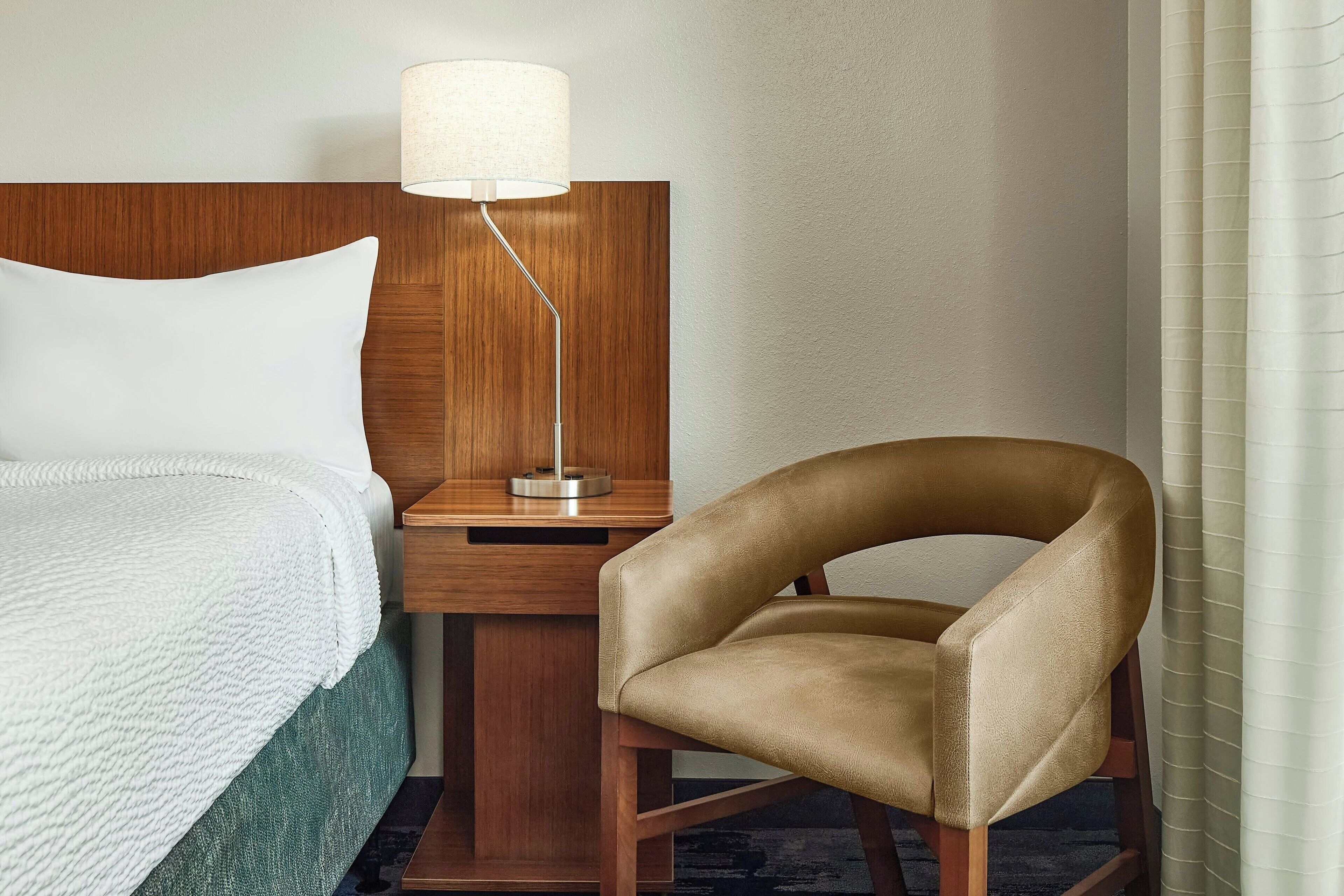 A hotel room with a bed, a nightstand, a lamp, and a chair.