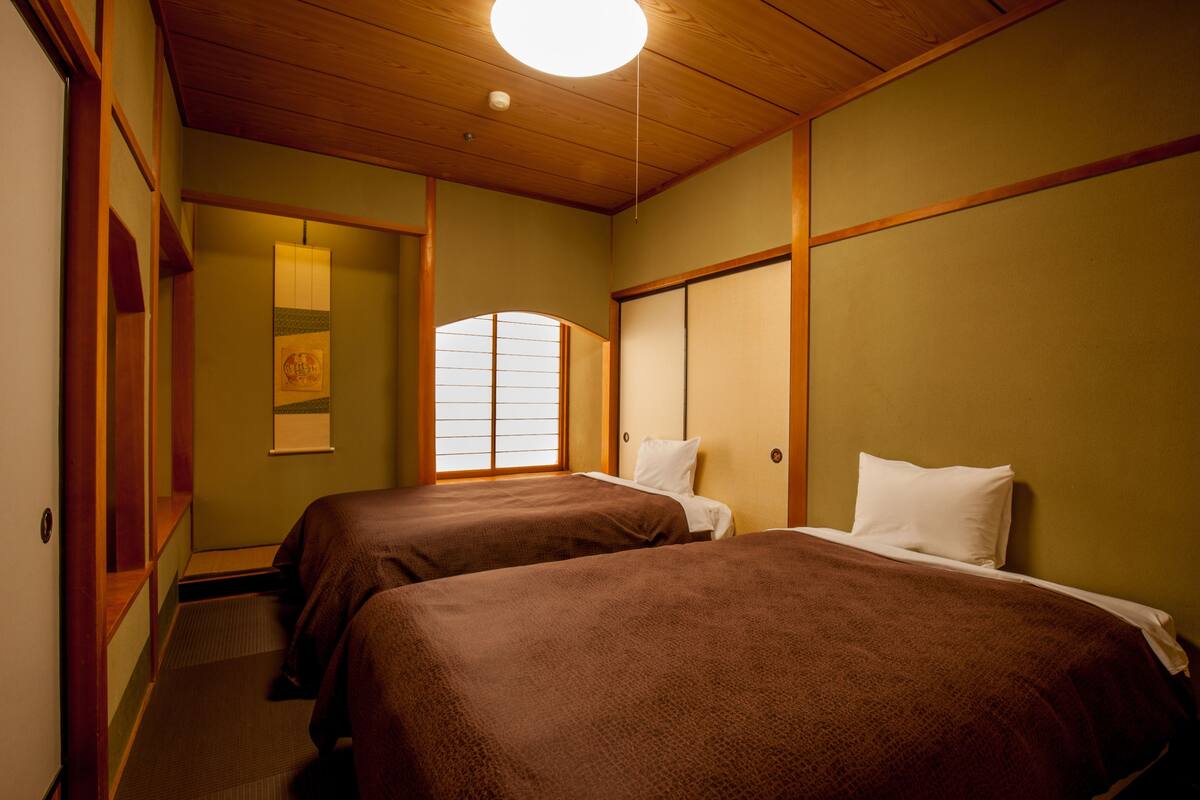 A room with two beds, wooden paneling, a shoji screen window, and a ceiling light.