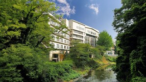A riverside building with multiple floors, surrounded by lush greenery. - Select Grand Kagayamanaka (Kaga)