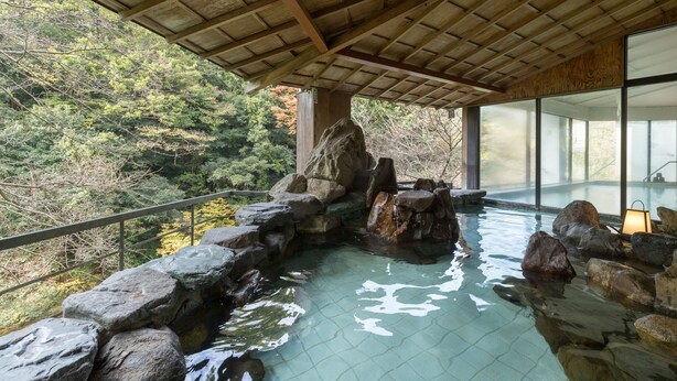 A hot spring area with a wooden ceiling, large rocks, and a view of trees. - Select Grand Kagayamanaka (Kaga)