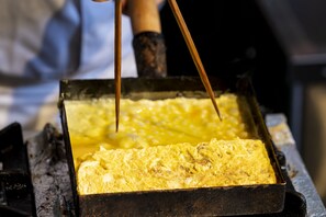 A rectangular metal tray with a yellow, textured substance, possibly food, being handled with chopsticks.